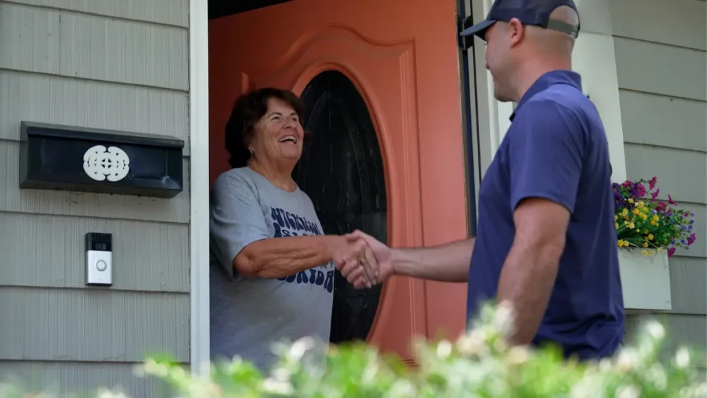 A technician from Jeremy Electrical shaking hands with a homeowner at her front door after completing a project.